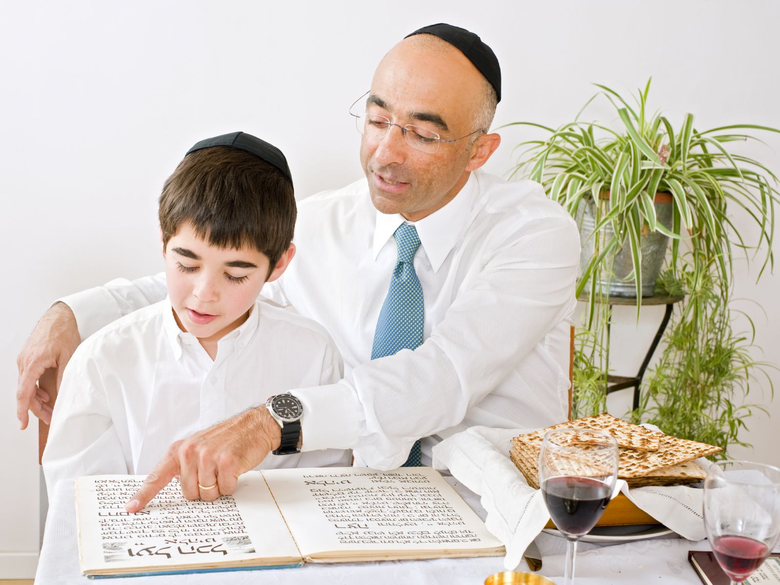 A Jewish father reads a Hebrew Haggadah with his son during the Passover Seder.