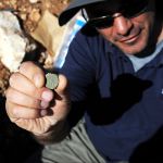 IAA archaeologist Pablo Betzer holds up a Jewish Revolt coin found outside Jerusalem