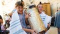 Two 13-year-old Jewish boys share the weight of carrying a Torah scroll encased by a silver Torah tik.