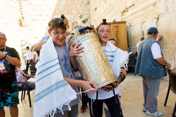 Two 13-year-old Jewish boys share the weight of carrying a Torah scroll encased by a silver Torah tik.