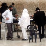 Israeli Jewish men have a discussion around a table full of Jewish prayer books, Scripture, and other reading material at the Western Wall.