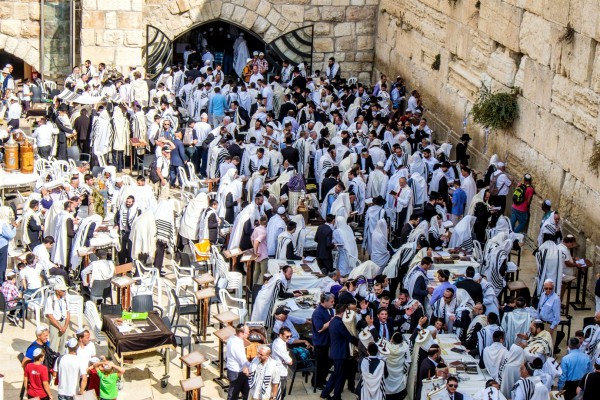 Men gather to worship God at the Western (Wailing) Wall. On close inspection, at least 20 Torah scrolls are either being carried or are placed on tables in the above photo.