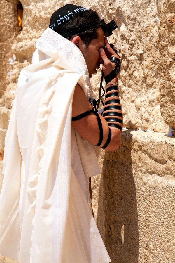 A Jewish man prays at the Wailing (Wailing) Wall in the Old City of Jerusalem wearing a tallit (prayer shawl), a kippah (head covering), and tefillin (phylacteries). (Israeli Ministry of Tourism photo by Noam Chen)