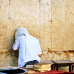 A Jewish man prays at the Western (Wailing) Wall with his tallit (prayer shawl) pulled over his head.