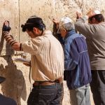 Siddur-Jewish prayer at the Western (Wailing) Wall in Jerusalem. The man wearing tefillin (phylacteries) is reading from a Siddur.