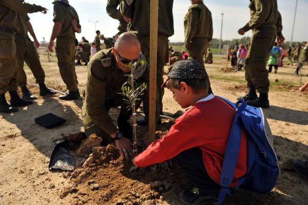 An Israel Defense Forces solder helps a child plant a tree for Tu B'Shvat.