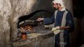 Man bakes bread at a recreated home in Nazareth, wearing period clothes from the time of Yeshua.