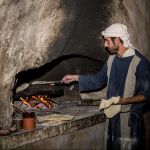 Man bakes bread at a recreated home in Nazareth, wearing period clothes from the time of Yeshua.