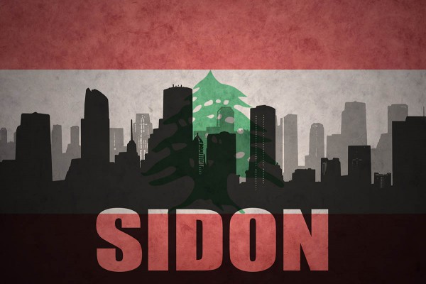 Silhoutte of Sidon skyline with flag of Lebanon in the background.